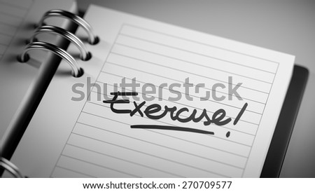 Closeup of a personal agenda setting an important date representing a time schedule. The words Exercise! written on a white notebook to remind you an important appointment.
