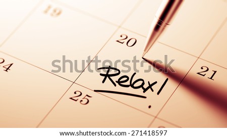 Closeup of a personal agenda setting an important date written with pen. The words Relax written on a white notebook to remind you an important appointment.