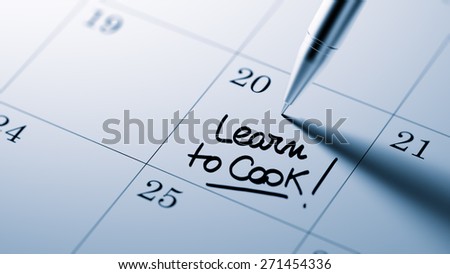 Closeup of a personal agenda setting an important date written with pen. The words Learn to Cook written on a white notebook to remind you an important appointment.