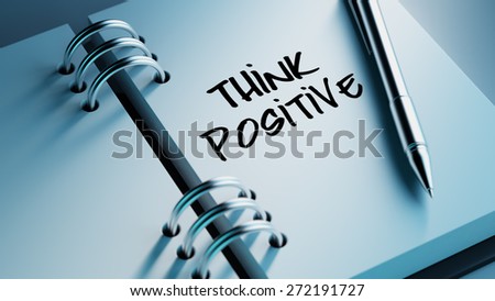 Closeup of a personal agenda setting an important date writing with pen. The words Think positive written on a white notebook to remind you an important appointment.
