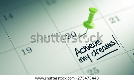 Concept image of a Calendar with a green push pin. Closeup shot of a thumbtack attached. The words Achieve my dreams written on a white notebook to remind you an important appointment.