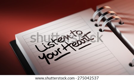 Closeup of a personal agenda setting an important date representing a time schedule. The words Listen to your heart written on a white notebook to remind you an important appointment.
