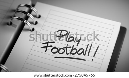 Closeup of a personal agenda setting an important date representing a time schedule. The words Play Football written on a white notebook to remind you an important appointment.