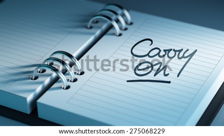 Closeup of a personal agenda setting an important date representing a time schedule. The words Carry on written on a white notebook to remind you an important appointment.