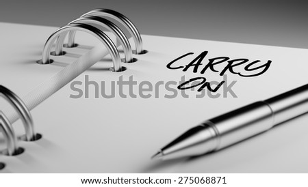 Closeup of a personal agenda setting an important date writing with pen. The words Carry on written on a white notebook to remind you an important appointment.