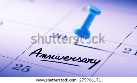 Concept image of a Calendar with a blue push pin. Closeup shot of a thumbtack attached. The words Anniversary written on a white notebook to remind you an important appointment.
