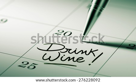 Closeup of a personal agenda setting an important date written with pen. The words Drink Wine written on a white notebook to remind you an important appointment.