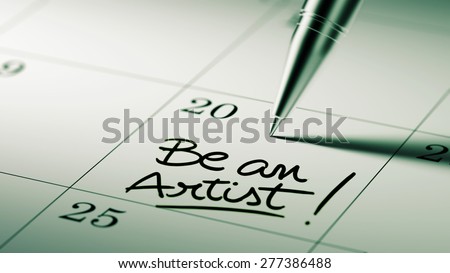 Closeup of a personal agenda setting an important date written with pen. The words Be an Artist written on a white notebook to remind you an important appointment.