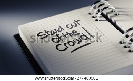 Closeup of a personal agenda setting an important date representing a time schedule. The words Stand out of the crowd written on a white notebook to remind you an important appointment.