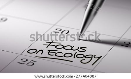 Closeup of a personal agenda setting an important date written with pen. The words Focus on Ecology written on a white notebook to remind you an important appointment.