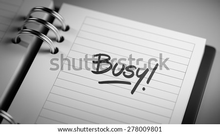 Closeup of a personal agenda setting an important date representing a time schedule. The words Busy written on a white notebook to remind you an important appointment.