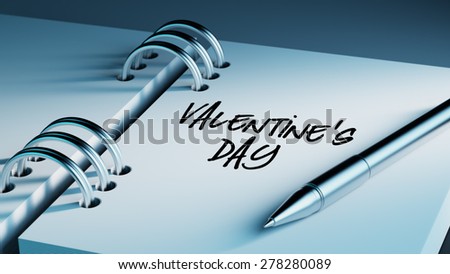 Closeup of a personal agenda setting an important date writing with pen. The words Valentine\'s Day written on a white notebook to remind you an important appointment.