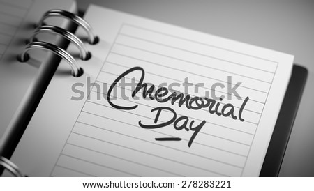 Closeup of a personal agenda setting an important date representing a time schedule. The words Memorial Day written on a white notebook to remind you an important appointment.
