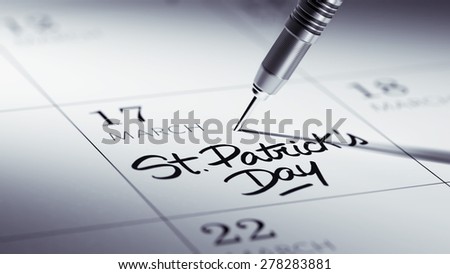 Concept image of a Calendar with a golden dart stick. The words St. Patrick\'s Day written on a white notebook to remind you an important appointment.