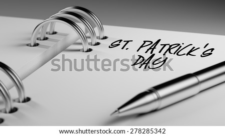 Closeup of a personal agenda setting an important date writing with pen. The words St. Patrick\'s Day written on a white notebook to remind you an important appointment.