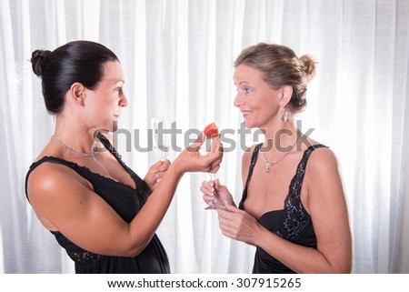 two attractive women - one is offering strawberry to her friend