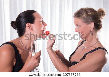 two attractive women - one is feeding the other with strawberry