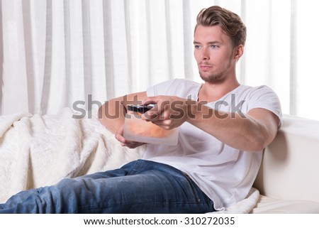 Portrait young man sitting on couch and eating chips and zapping TV