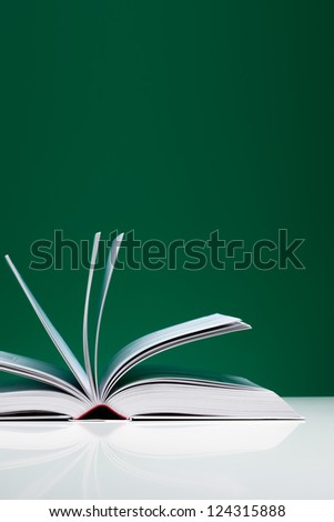 Single book on a white desk with flying pages over green background.