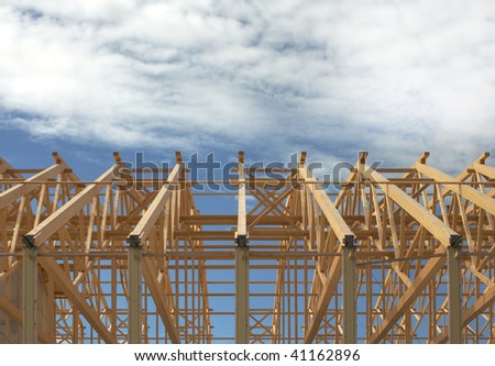 Wooden roof frame on a constructon site over blue sky with clouds.
