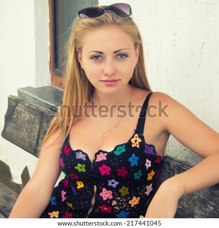 The photo shows a young beautiful girl. She sits on the bench. Her black skirt black blouse.