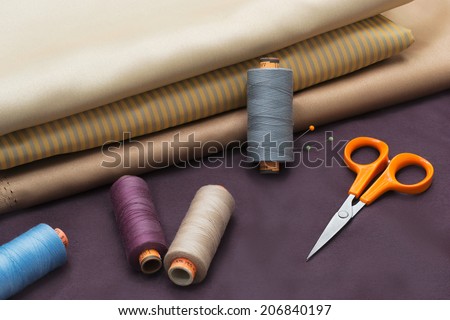 Different kind of fabric and tailors tools - thread spools, pin, scissors.