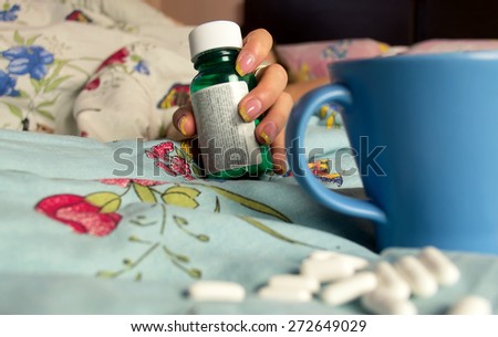 Female hand with medications pill bottles and spilled pills in the blurred foreground