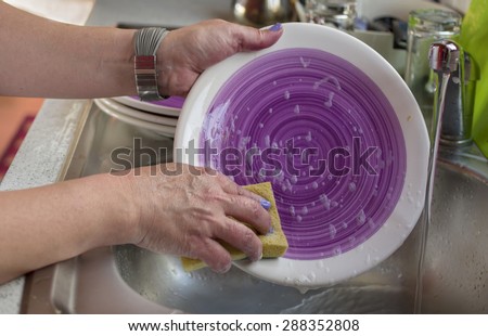 Closeup of female hands washing dish ware by spounge, indoor horizontal shot