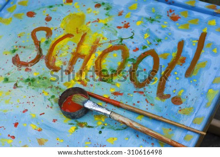 Closeup of the artist brushes laid on a desk painted in different colors, word School written in the image center