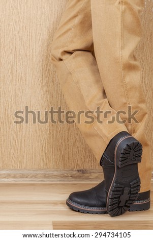 Men\'s leather shoes and jeans khaki legs. A man stands on a wooden floor near the wall.