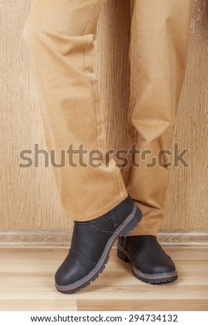 Men\'s leather shoes and jeans khaki legs. A man stands on a wooden floor near the wall.