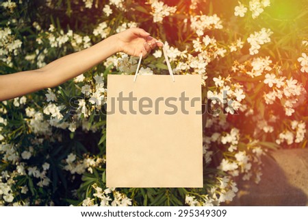 woman holding a bag on a background of flowers. flare light. paper bag in hands