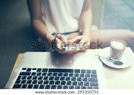 girl working at a computer and holding a phone in his hand. focus on phone and laptop keyboard. flare light, cross process.