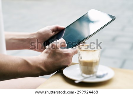 Woman uses a digital tablet in coffee shop. Coffee on the table. Close up to view young woman\'s hands hold tablet