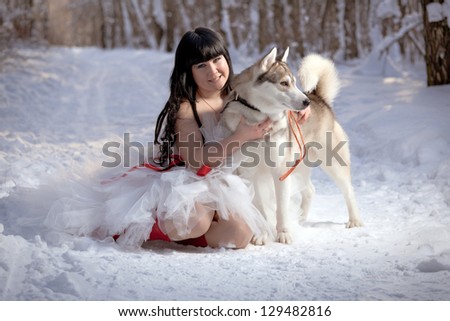 The young  oriental  woman in white sumptuous dress  sits with  husky dog in the winter forest