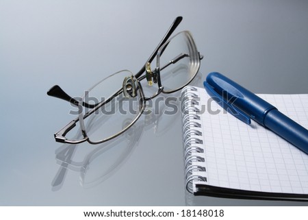 Close-up of spectacles with notebook and pen