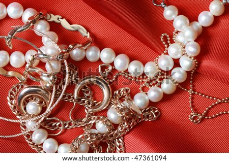 Pearl necklace and gold jewelry lying on red silk background with copy space