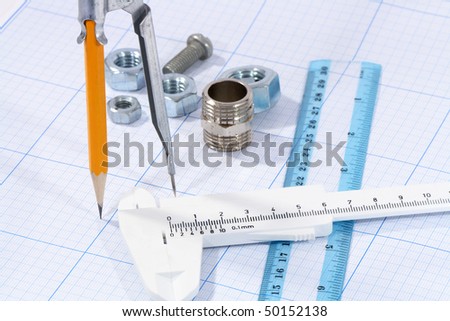 Divider, pencil, caliper, ruler and few screw nuts on graph paper background