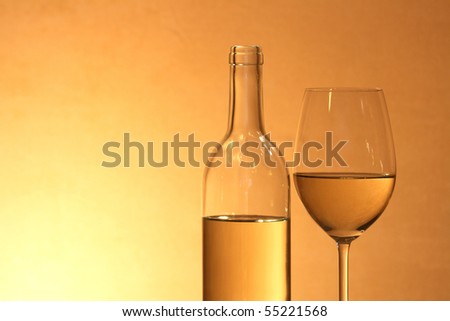 Wineglass near bottle of white wine on red-yellow background with copy space