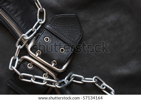 Metal chain lying on black leather background with clasp and zipper