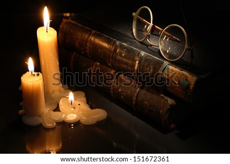 Vintage still life with lighting candles near books on dark background