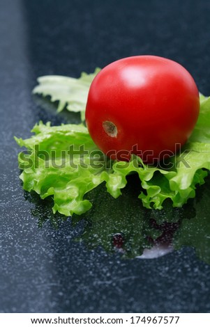 One red tomato and green salad leaf on dark background