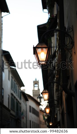 Evening street in Florence. Few glowing vintage street lamps on background with buildings and tower
