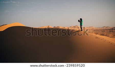 One person on a dune in the desert, holding a touch pad. Landscape