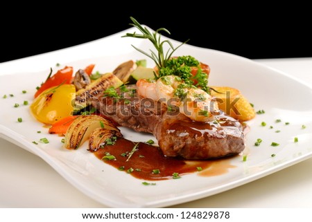 Delicious juicy barbequed steak and prawns with grilled tomato and roasted potatoes. Surf and Turf style. Shallow dof