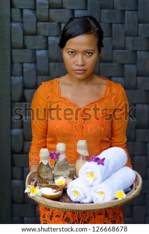 Massage therapist at the luxury Spa on Bali Island holding tray with: Massage oil, bath salt, body scrub, Towels,Cinnamon sticks, Orchids and frangipani flowers