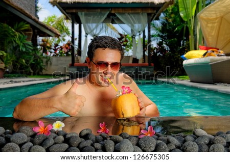 Relaxing on holiday, Handsome man with thumbs up relaxing in swimming pool and drinking coconut cocktail in luxury villa on Bali island