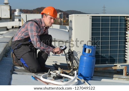 Air Conditioning Repair, young repairman on the roof fixing air conditioning system. Model is actual electrician.
