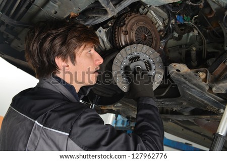 Auto mechanic working under the car and changing clutch at car repair shop