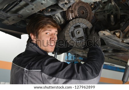Auto mechanic working under the car and changing clutch at car repair shop